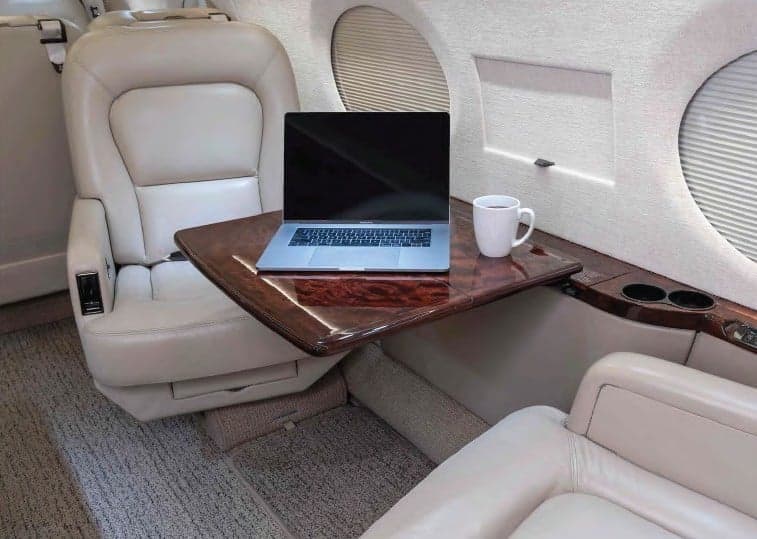 Interior view of the aircraft with a laptop and coffee on a table.