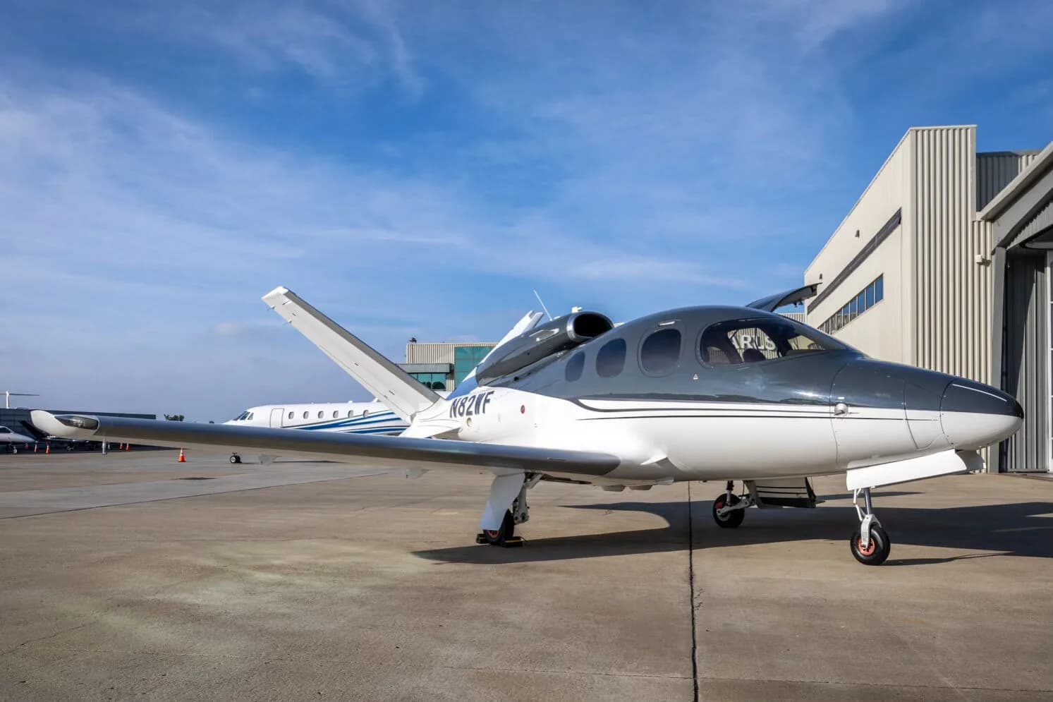 A three-quarter front view of a white and dark grey Cirrus Vision Jet (N82WF) parked outside a hangar.