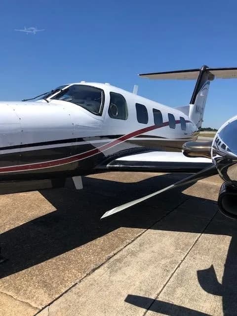 A close-up side view of a white and dark grey twin-engine turboprop aircraft with red pinstripes, tail number N444CY, parked on a tarmac.