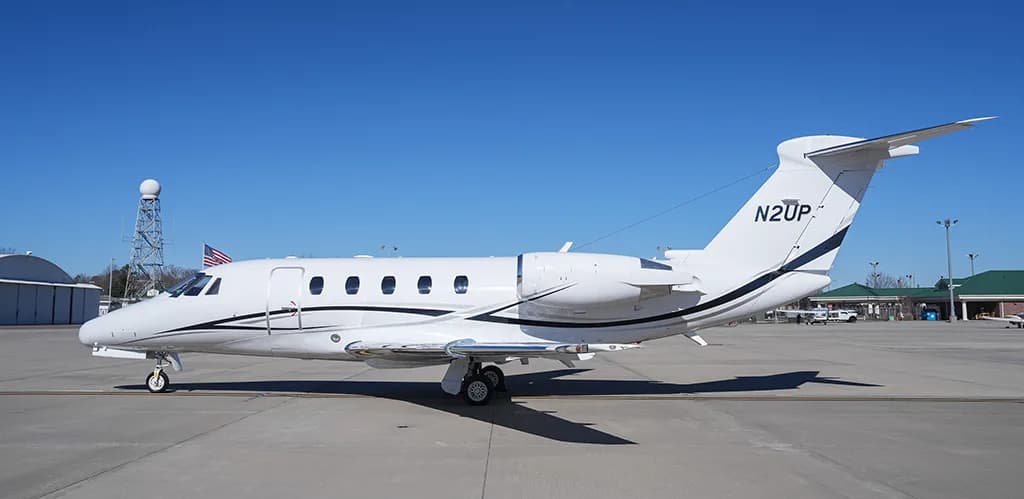 A white Cessna Citation business jet with black and grey stripes, registration N2UP, parked on an airfield.