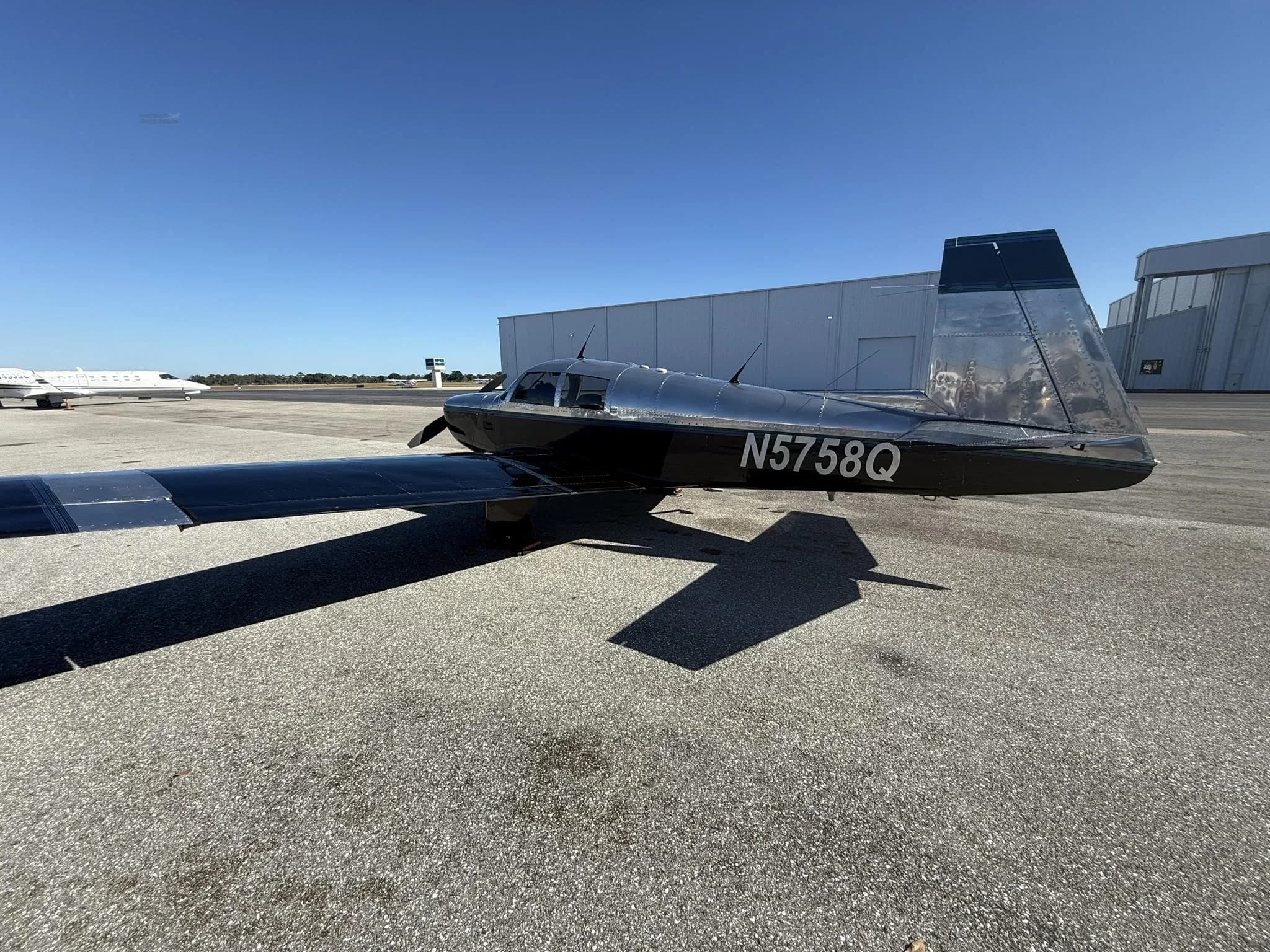 A black and silver Mooney M20 aircraft, N5758Q, parked on an asphalt tarmac with its tail facing right.