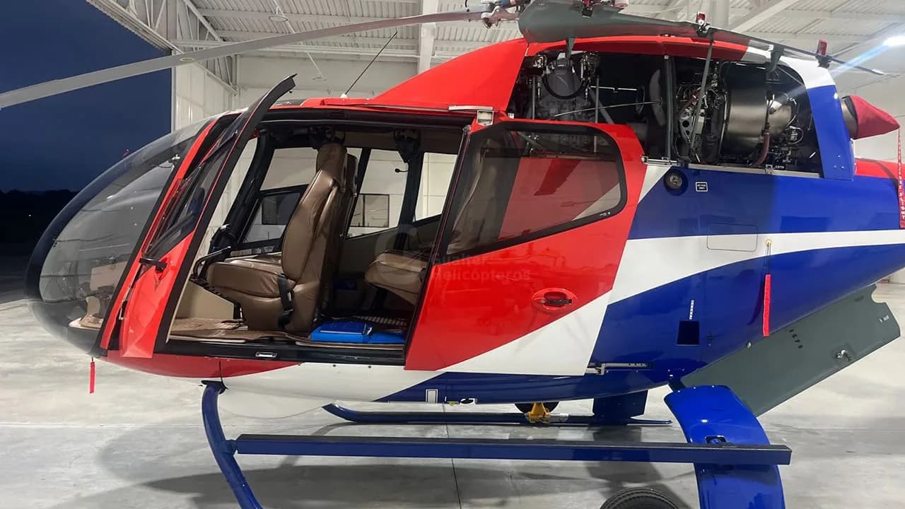 A red, white, and blue helicopter with its doors open reveals the interior and engine compartment in a hangar.