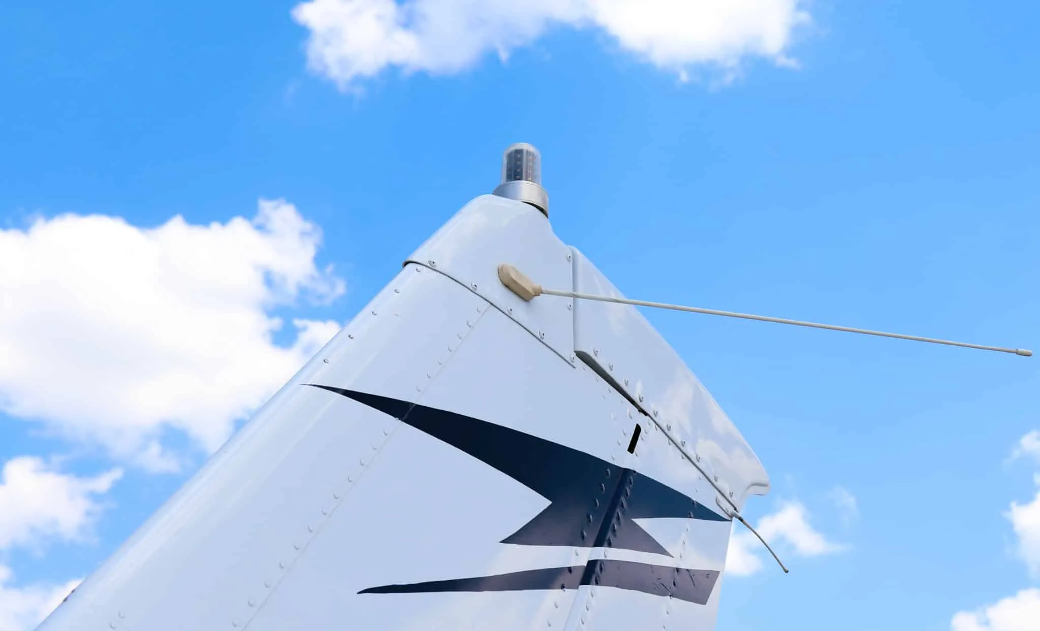 A close-up of the vertical stabilizer of a white Cessna 182 Skylane against a blue sky.
