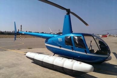 A blue Robinson R44 helicopter with floats parked on a tarmac.