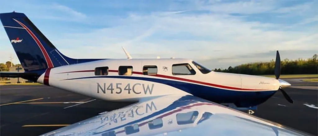 A side view of the Piper Matrix N454CW aircraft on an airfield, showing its white, blue, and red livery.