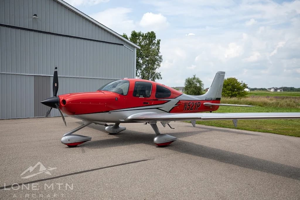 A red and silver Cirrus SR22 aircraft, N521P, parked on an asphalt ramp with a hangar in the background.