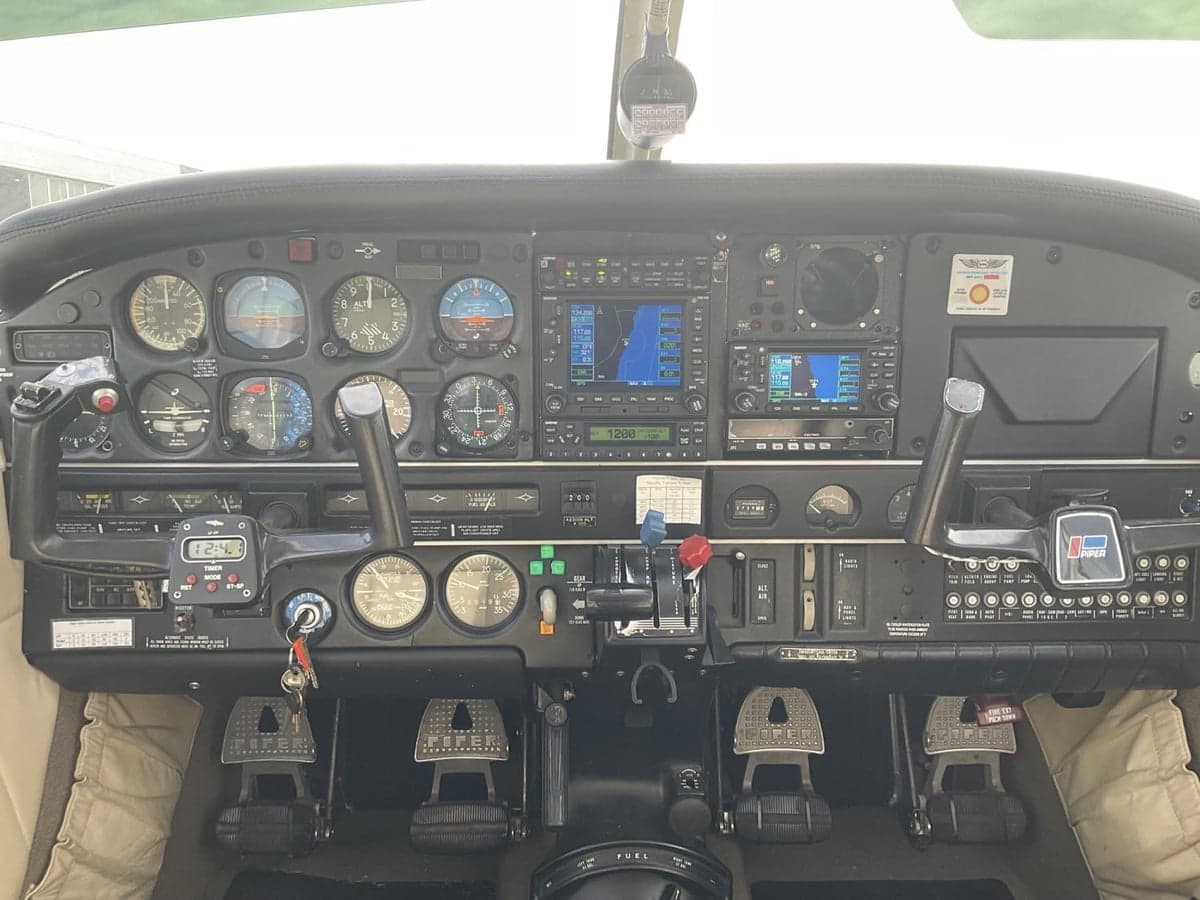 The cockpit of a Piper Saratoga aircraft showing the instrument panel with analog gauges and digital displays.