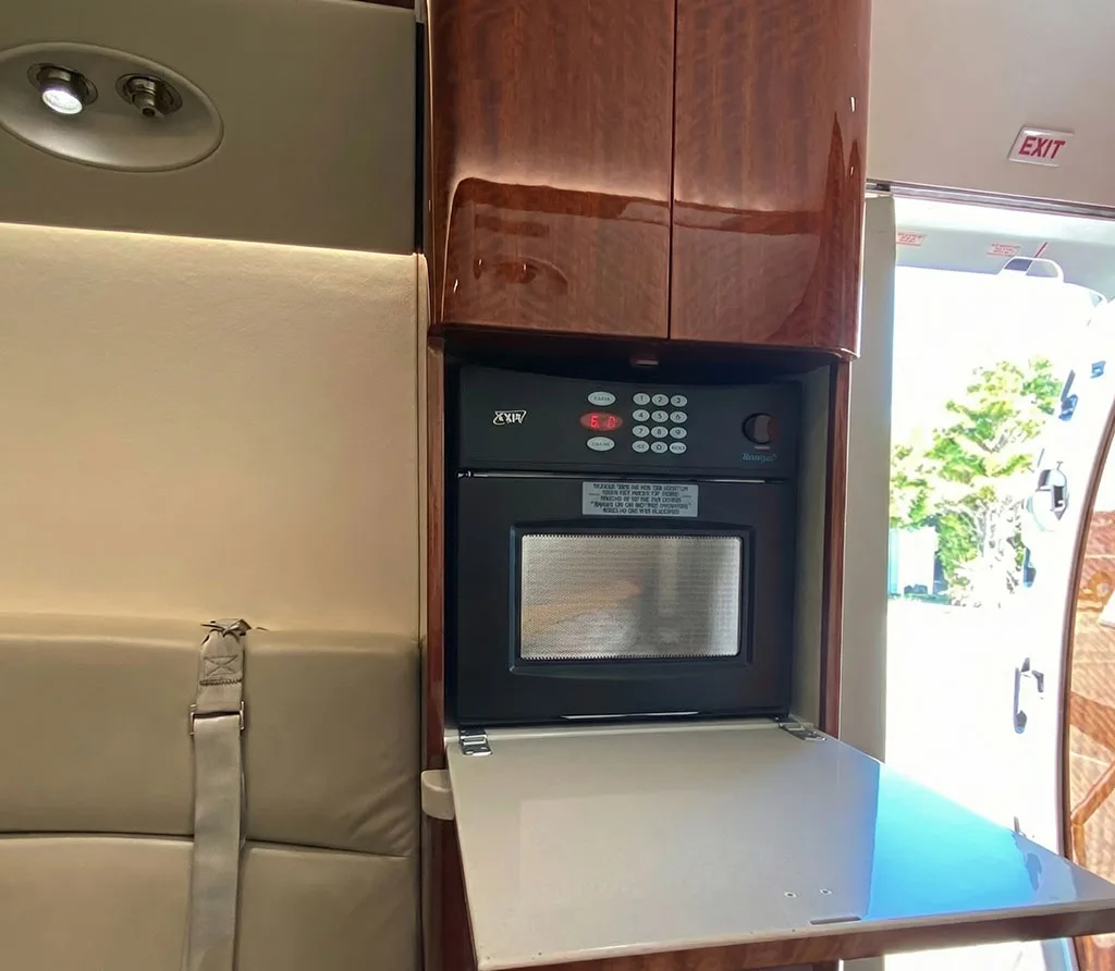 A galley area inside the aircraft features a built-in microwave oven and wooden cabinetry.