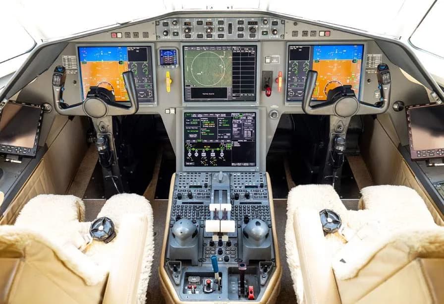 The modern cockpit of a business jet, featuring multiple digital displays and two pilot seats with sheepskin covers.