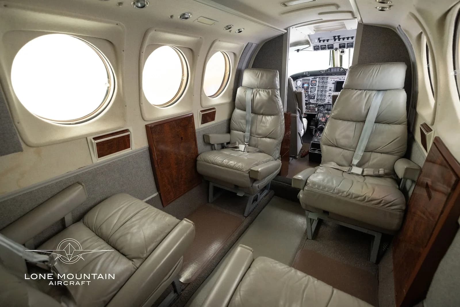 A side view of the aircraft's grey leather cabin seats, with a glimpse of the cockpit in the background.