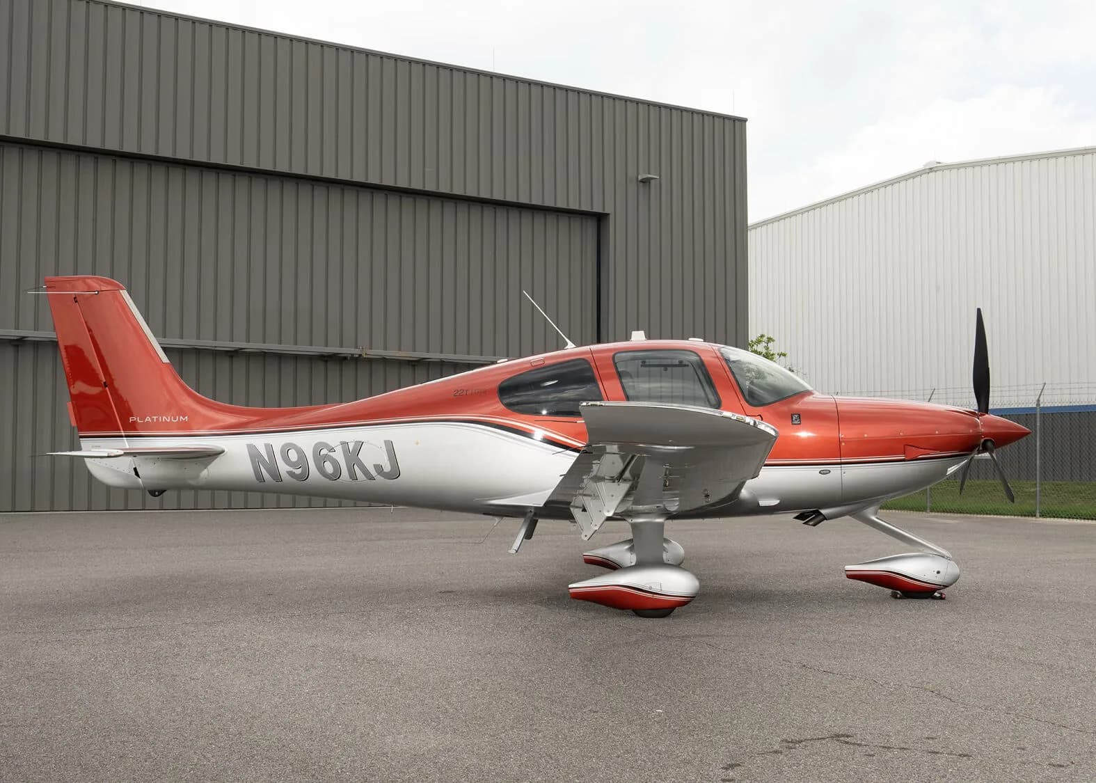 A red and silver Cirrus SR22T aircraft, registration N96KJ, parked on an asphalt apron in front of a hangar.