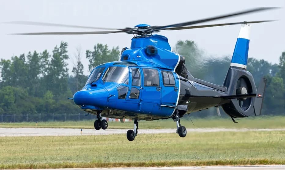 A blue and black helicopter taking off from a grassy field.