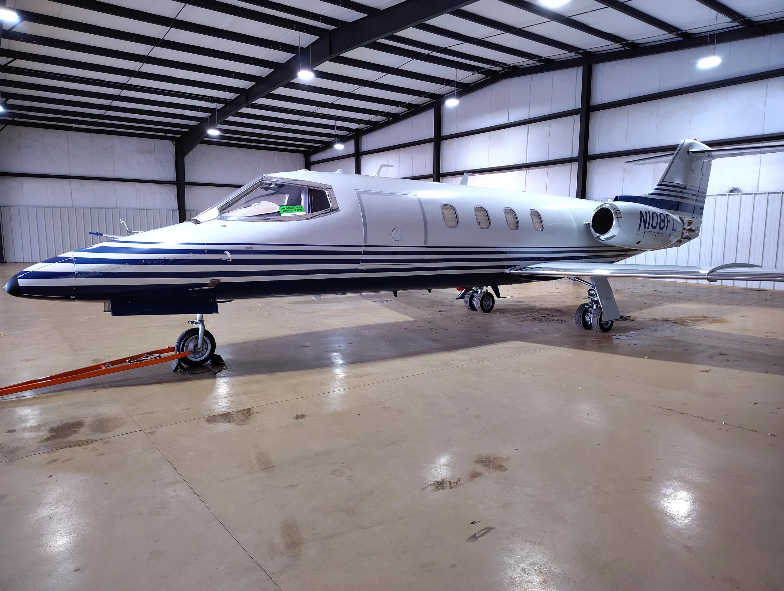 A Learjet aircraft with a white and blue stripe paint scheme viewed from the front-right inside a hangar.
