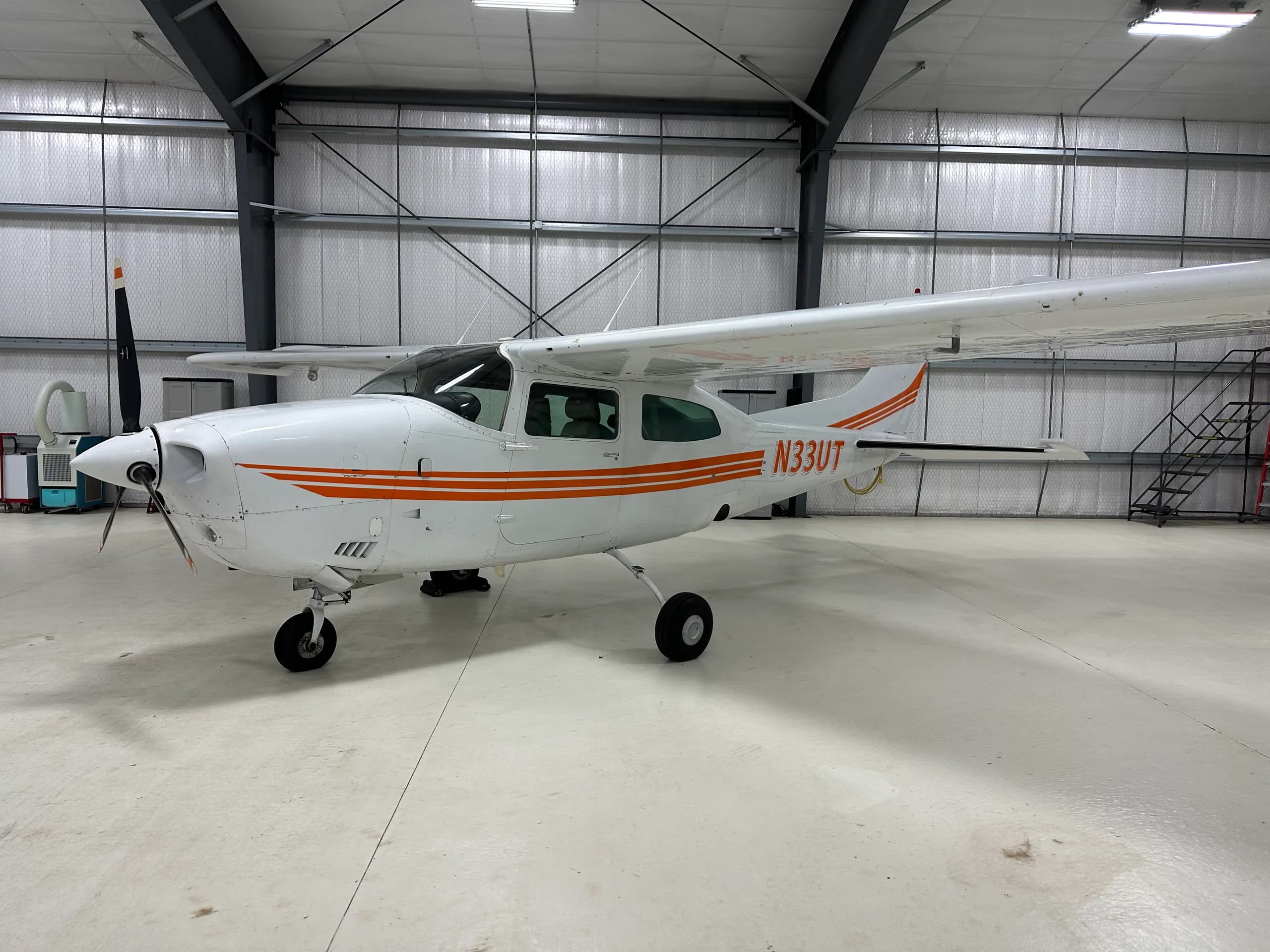A Cessna 206 Stationair aircraft with orange stripes parked in a hangar.