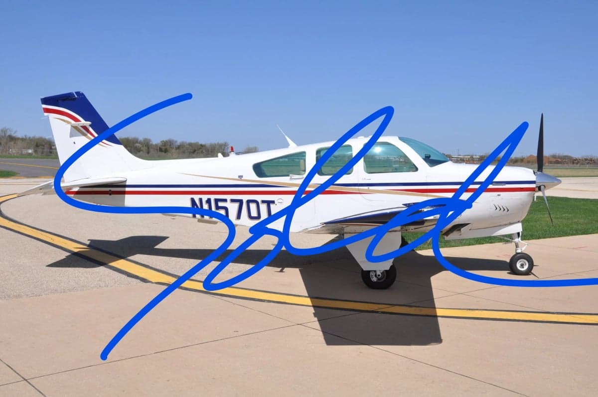 A Beechcraft Bonanza aircraft with a white and red paint scheme is parked on the tarmac.
