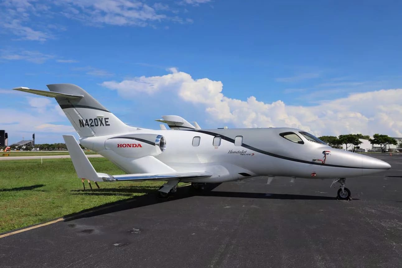 A white and grey HondaJet Elite S (N420XE) parked on a tarmac under a blue sky with clouds, viewed from the rear-right.