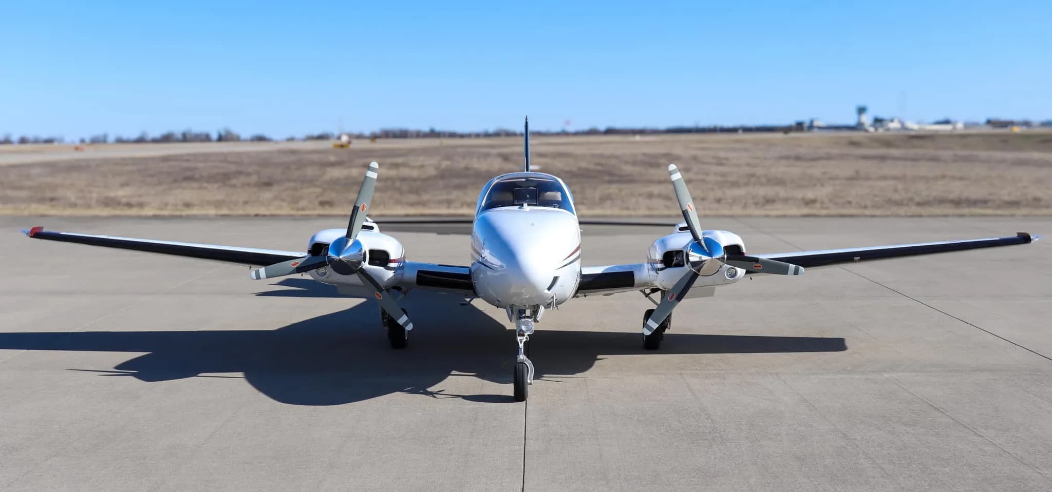 Head-on view of a white twin-engine Beechcraft Baron N204G with red, blue, and gray stripes, parked on an airfield.
