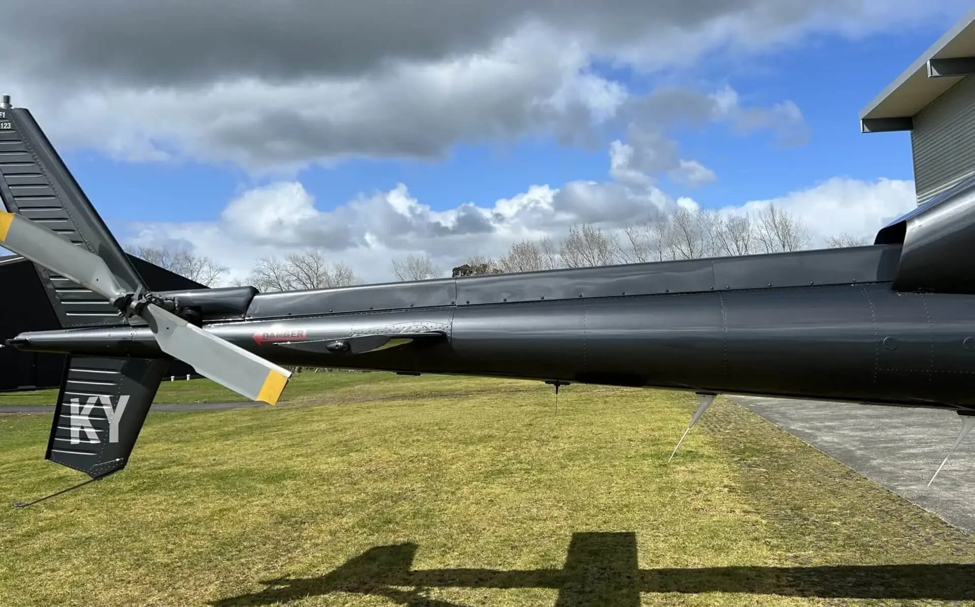 A close-up of the tail boom and tail rotor of a dark grey helicopter, showing the "KY" registration and a "DANGER" decal.