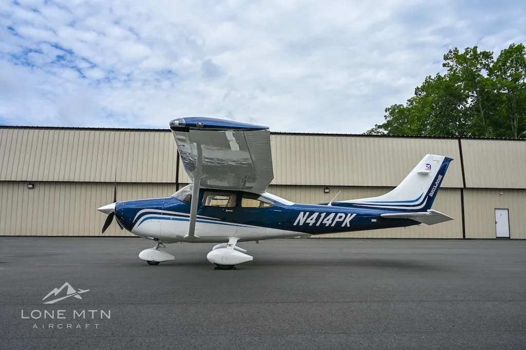 A side view of a blue and white Cessna Skylane N414PK with its wing flaps extended, parked on an asphalt ramp.