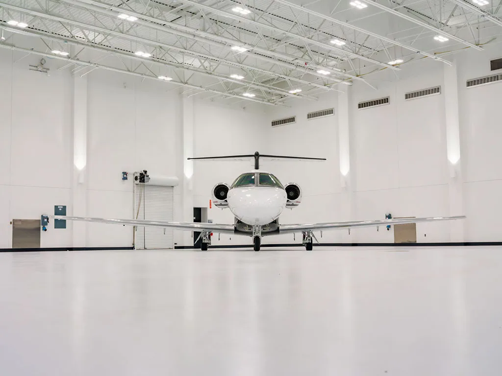 A head-on view of a white Cessna Citation Latitude business jet with black, red, and grey stripes parked in a brightly lit hangar.