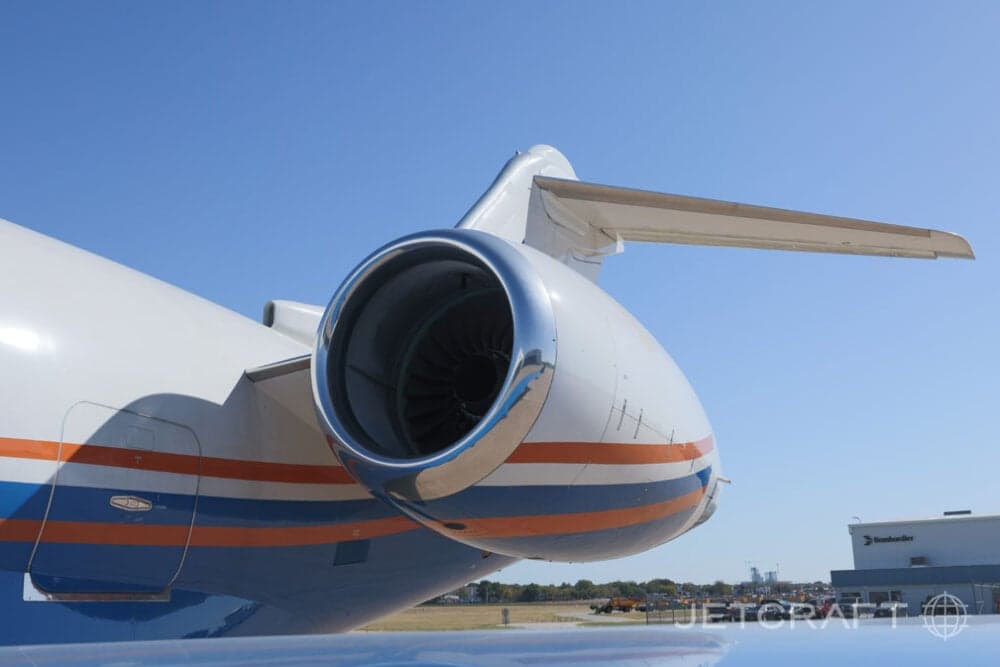 A close-up view of the rear engine and tail section of a white and blue business jet with orange stripes.