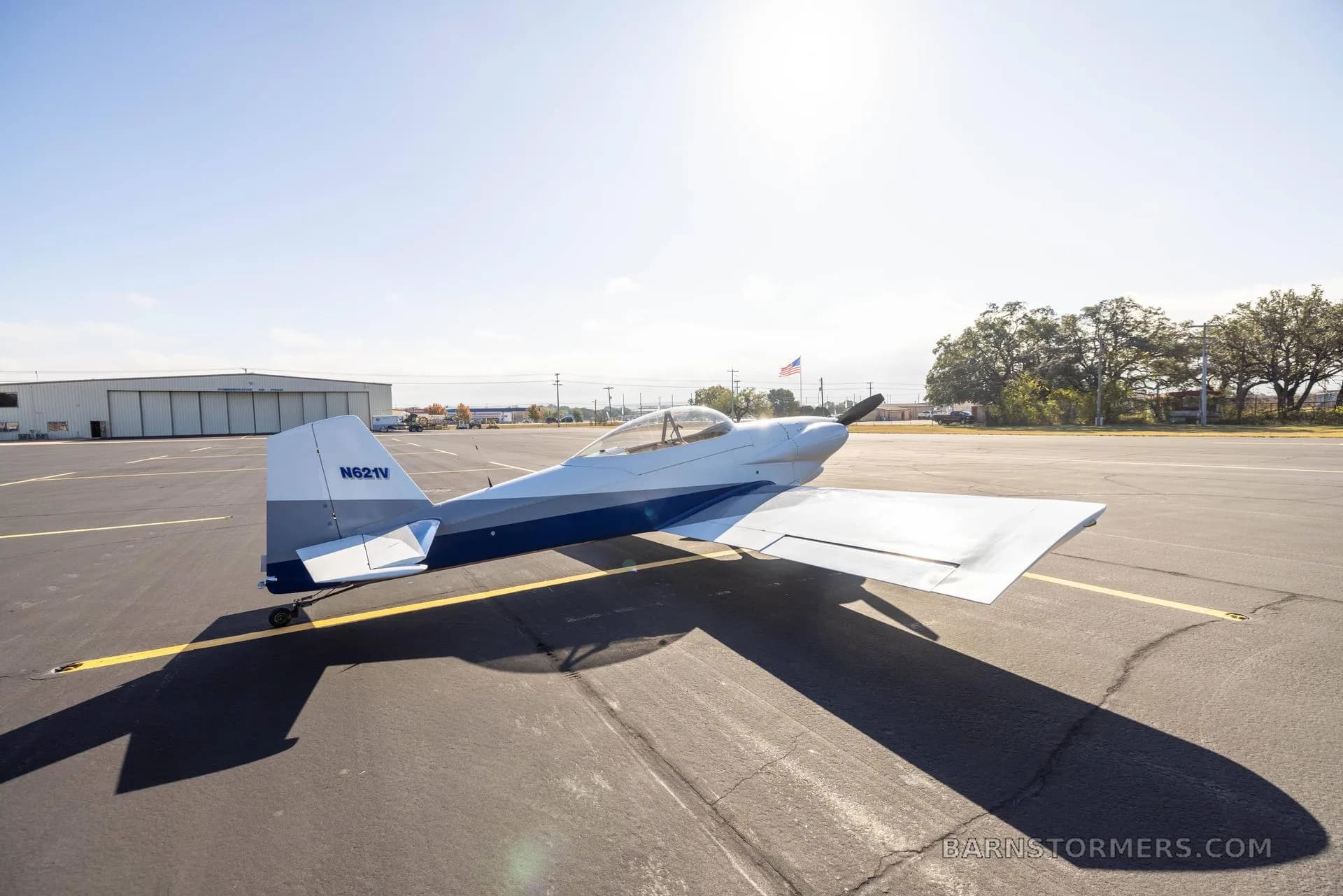 A white and blue single-engine aircraft with tail number N821V parked on an asphalt tarmac, viewed from the rear.