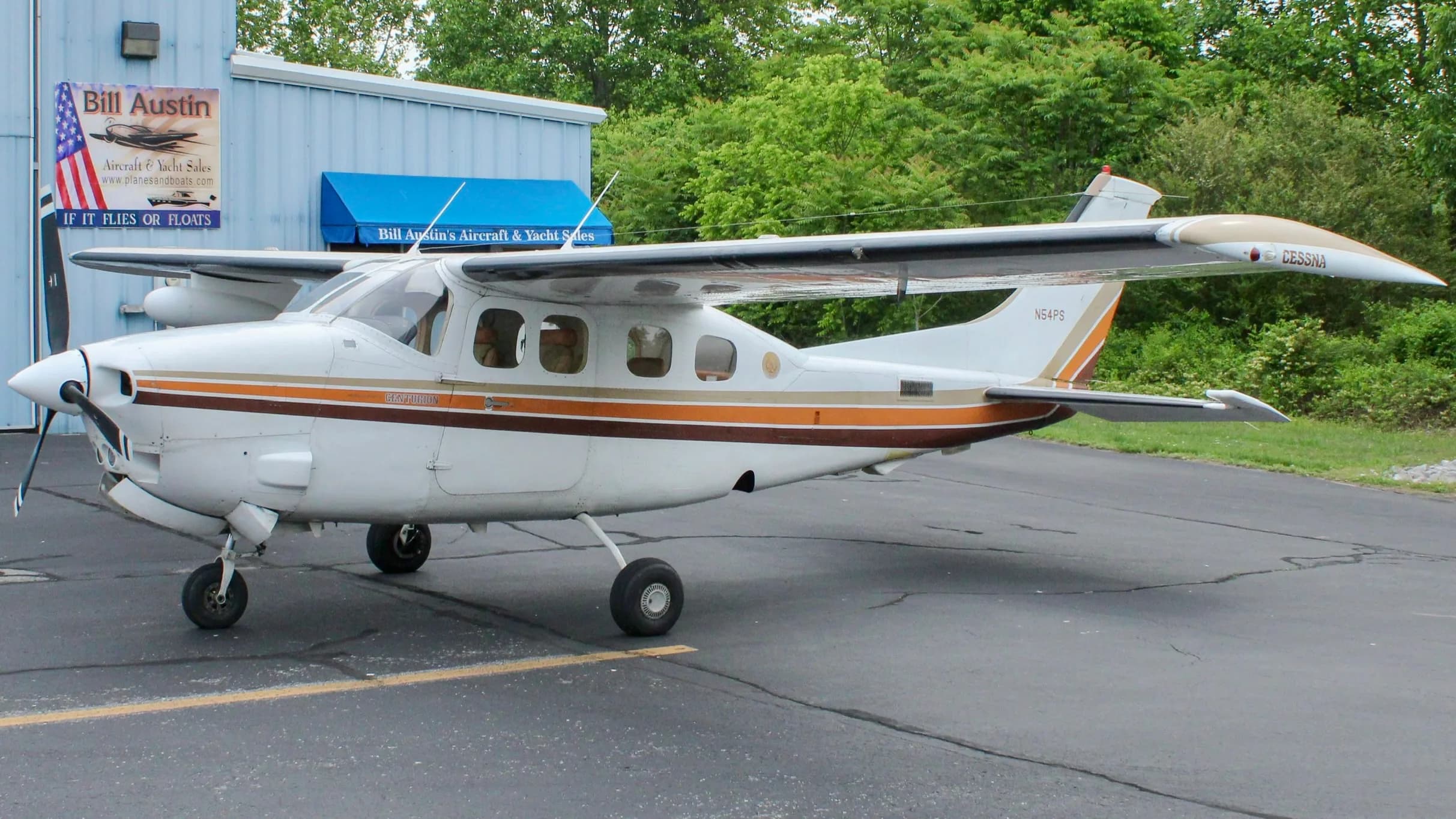 A white Cessna P210N Centurion with brown and orange stripes, registration N54PS, parked on an asphalt apron.