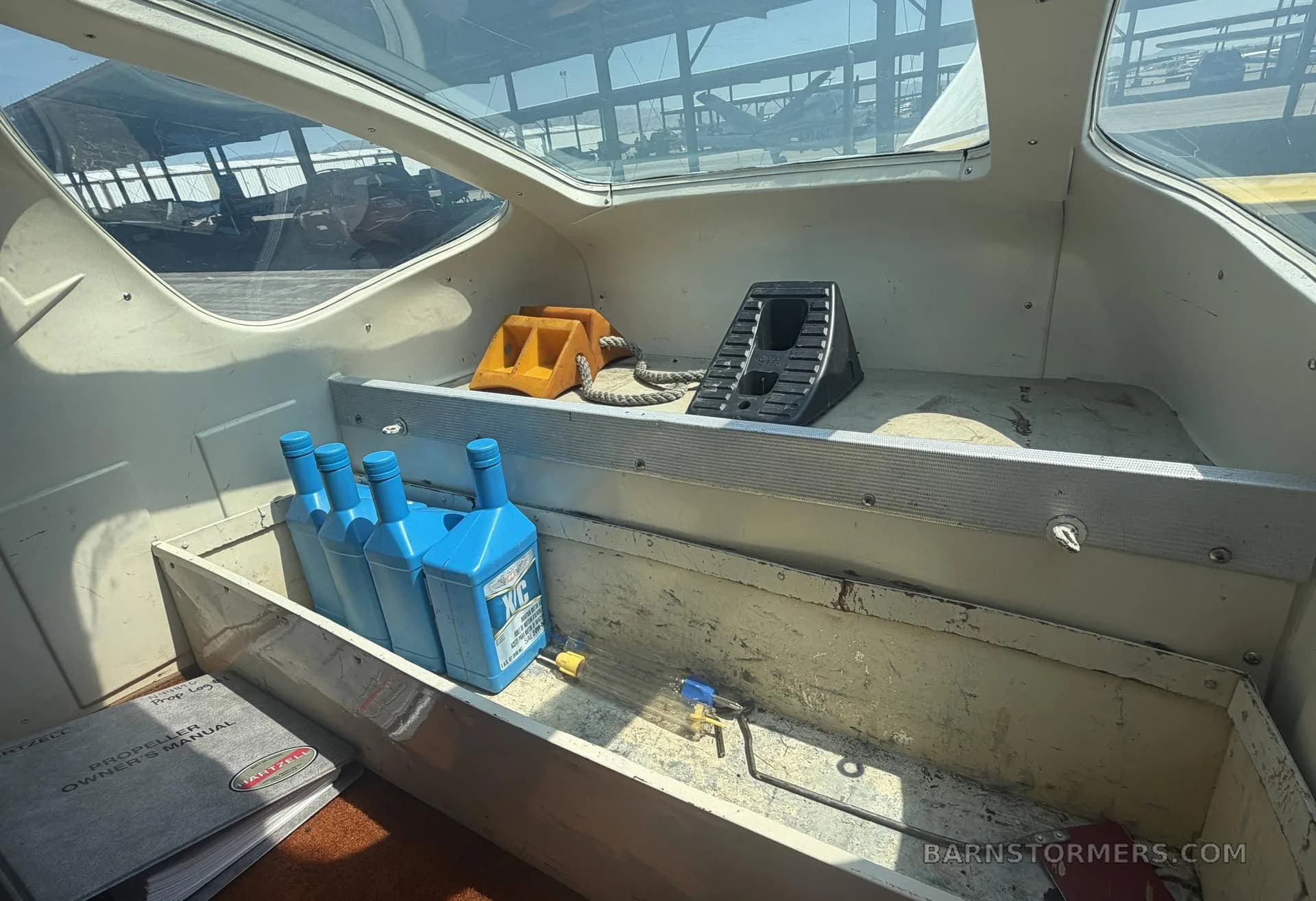 A close-up view of the aircraft's interior storage shelf, holding blue oil bottles and wheel chocks.
