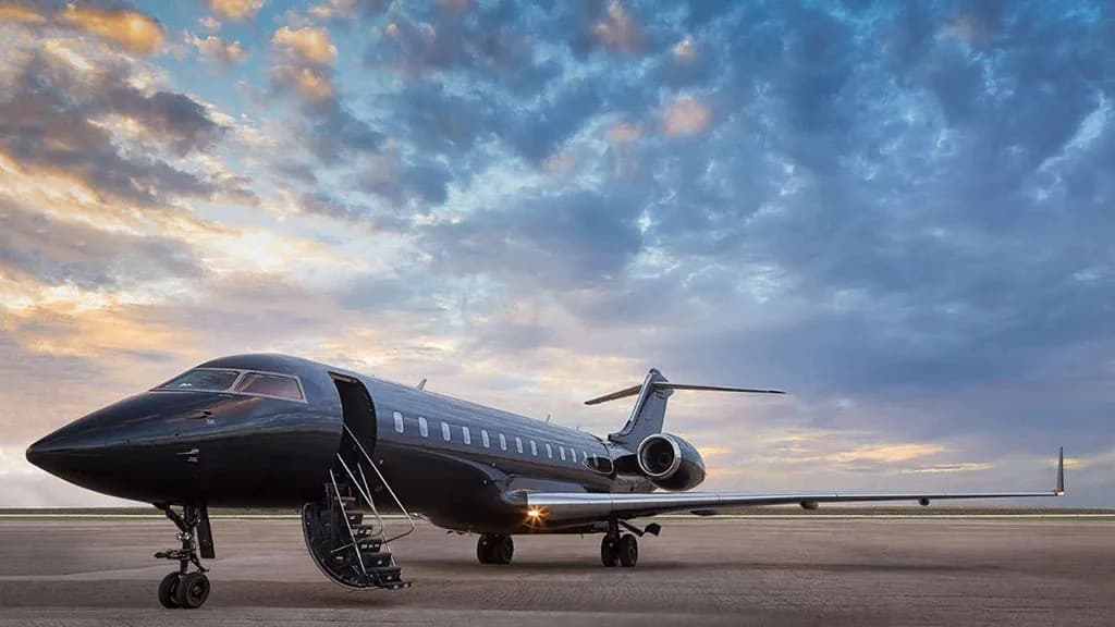 A sleek black business jet with its main door open, parked on an airfield under a dramatic cloudy sky at sunset.