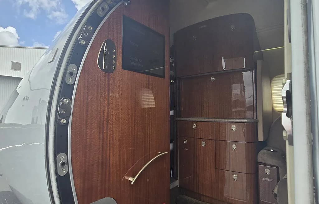 The interior entrance of a business jet, featuring rich wood paneling, a small display screen, and a storage cabinet.