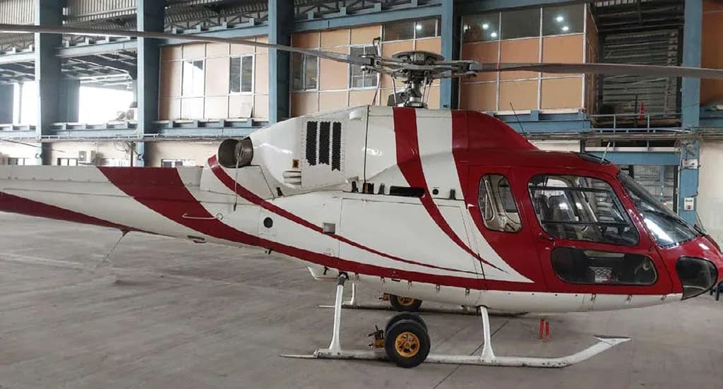 A close-up side view of a red and white helicopter with a striped paint scheme parked inside a hangar.