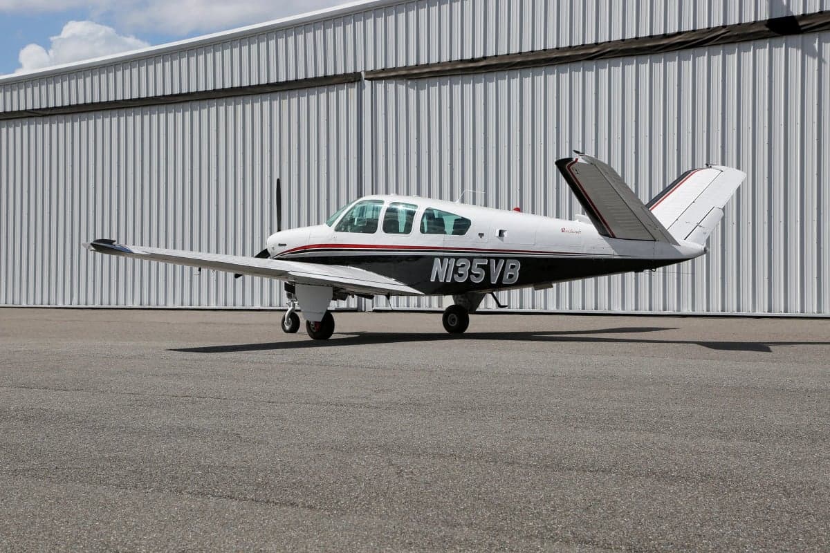 Side view of a Beechcraft Bonanza aircraft on the ground in front of a hangar, showing the tail number N135VB.