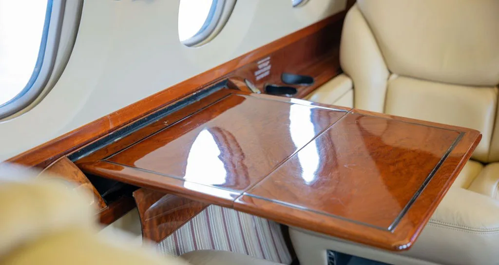 A close-up of a polished wooden fold-out table extended from the side panel in the private jet cabin.