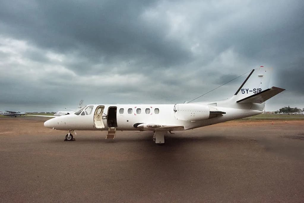 A white Cessna Citation business jet with registration 5Y-SIR parked on an airport tarmac with its cabin door open.