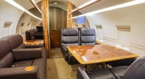 Interior of the Challenger aircraft cabin with leather seats and a wooden table.