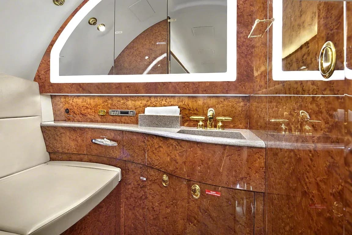 A close-up of the aircraft lavatory or galley with a sink, gold fixtures, and polished wood paneling.