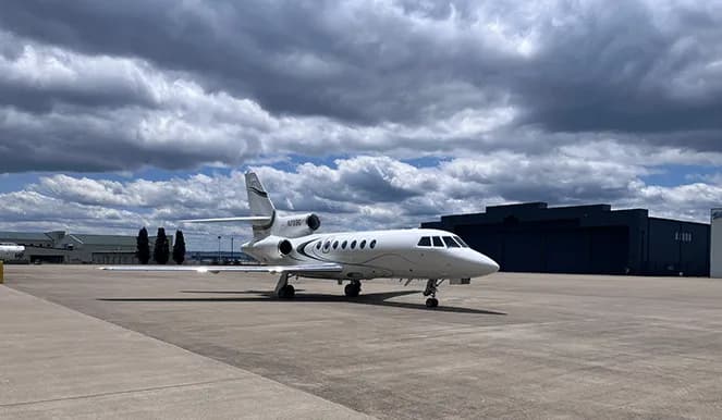 A white jet sits on the tarmac under a cloudy sky.