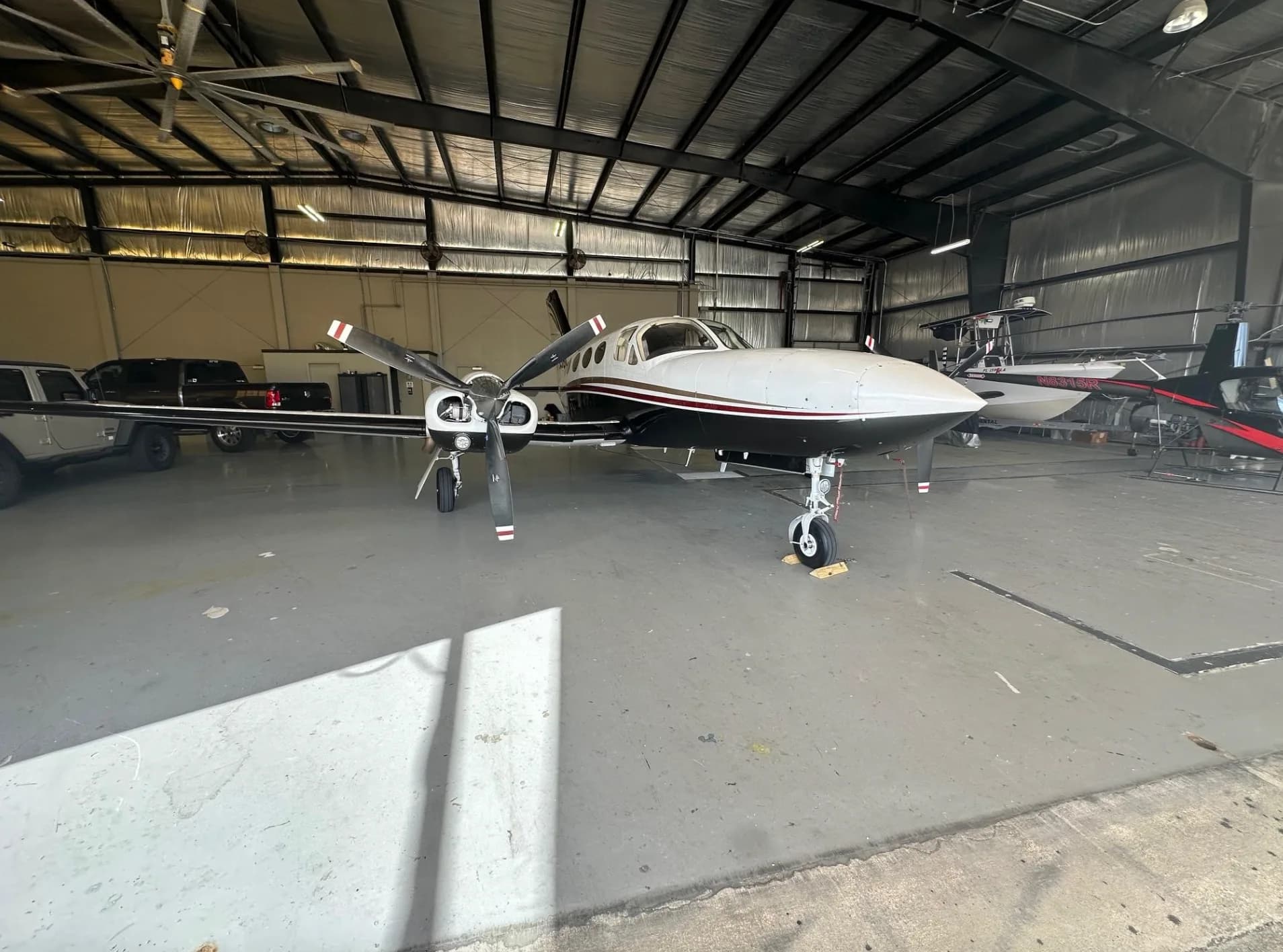 Front view of a white, black, and red twin-engine turboprop aircraft, N755BC, inside a hangar.