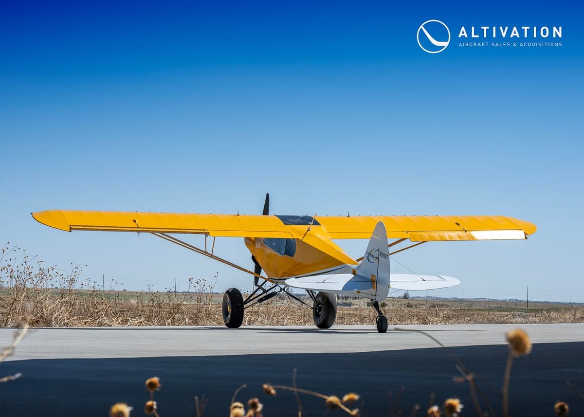 A yellow and white Carbon Cub aircraft parked on the tarmac, side view.