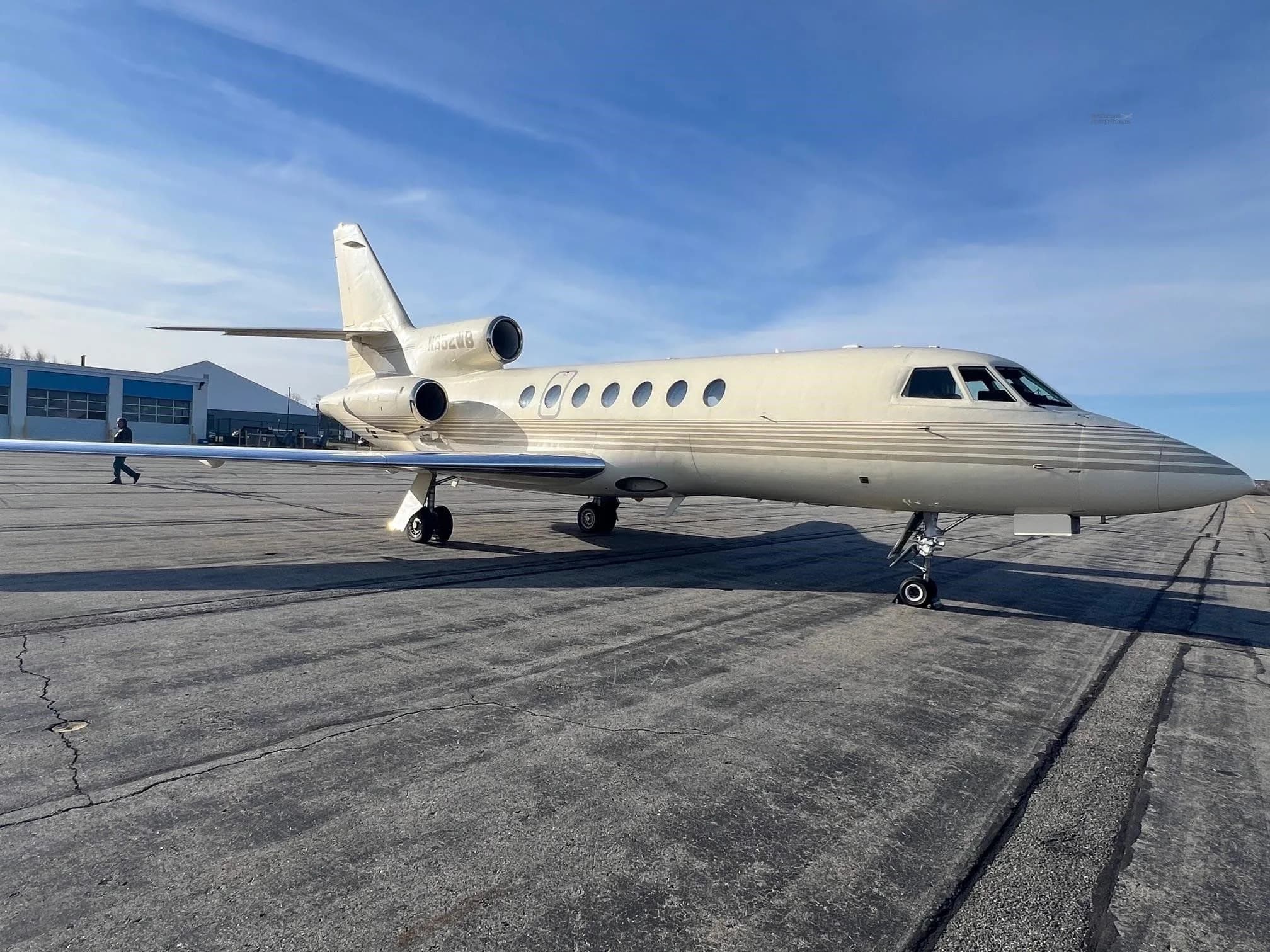 A beige Dassault Falcon 900EX business jet with N352WB registration on the tail, parked on an airport tarmac under a blue sky.