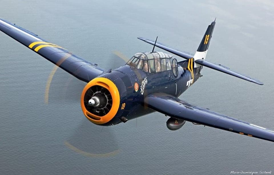 Grumman TBF Avenger in flight over water and land.