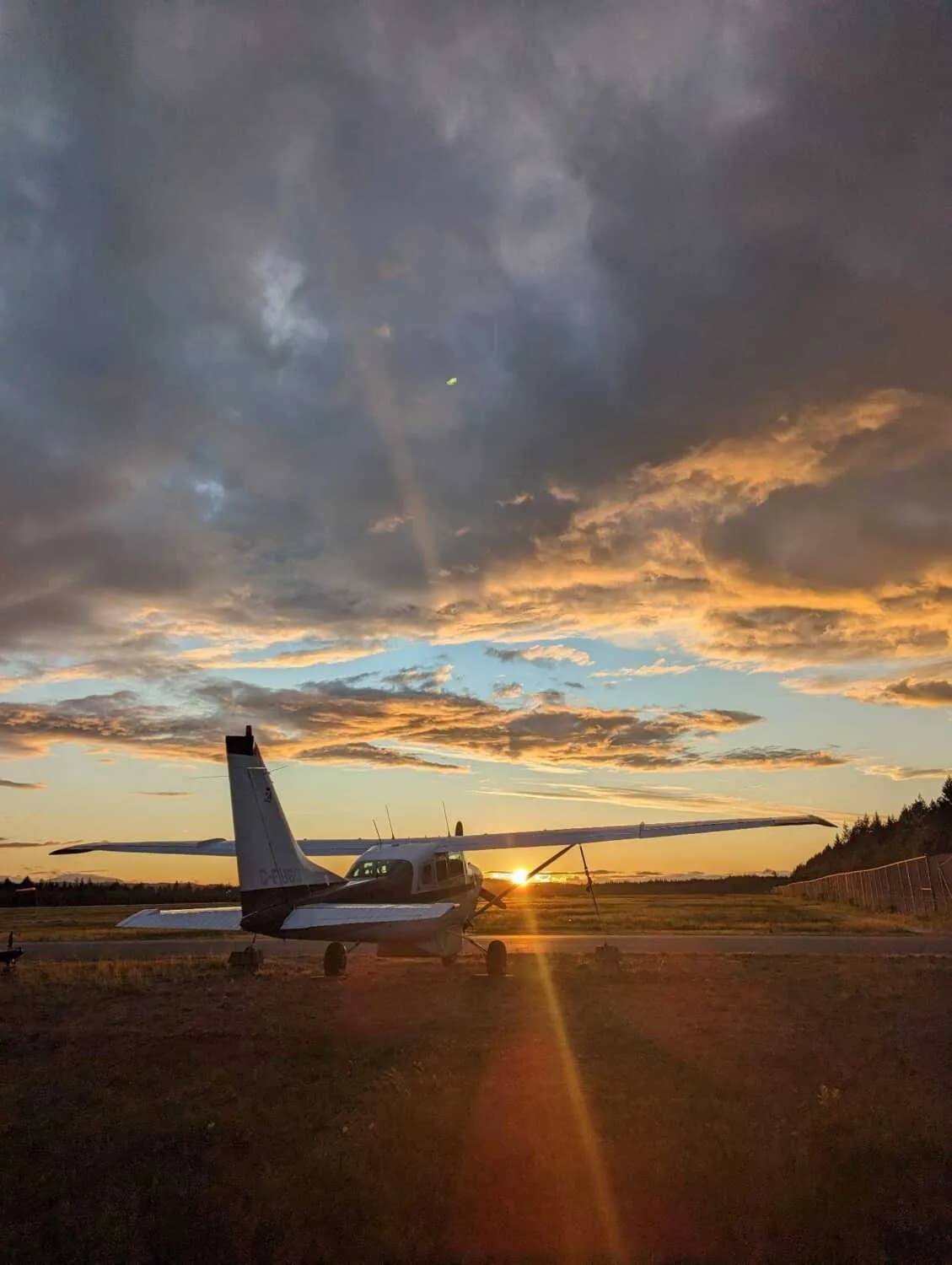 A Cessna 206 Stationair parked on a runway at sunset.