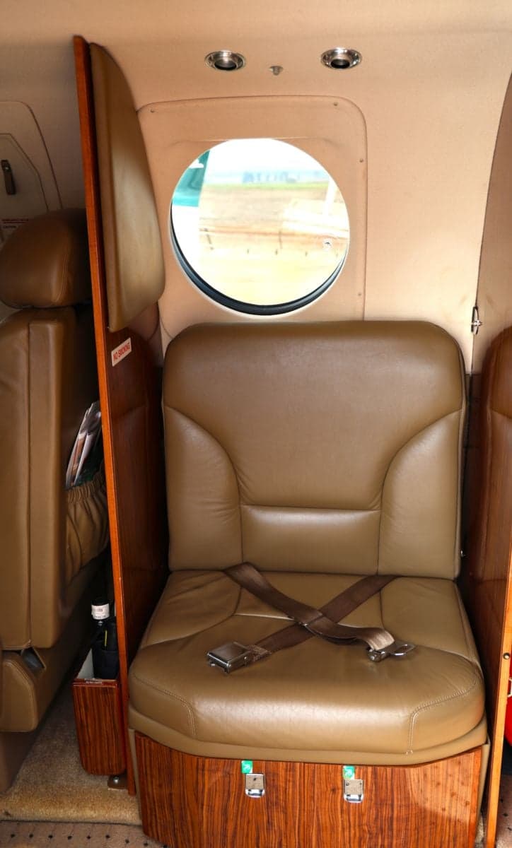 Interior view of an aircraft showing a leather seat with a seatbelt and a round window.