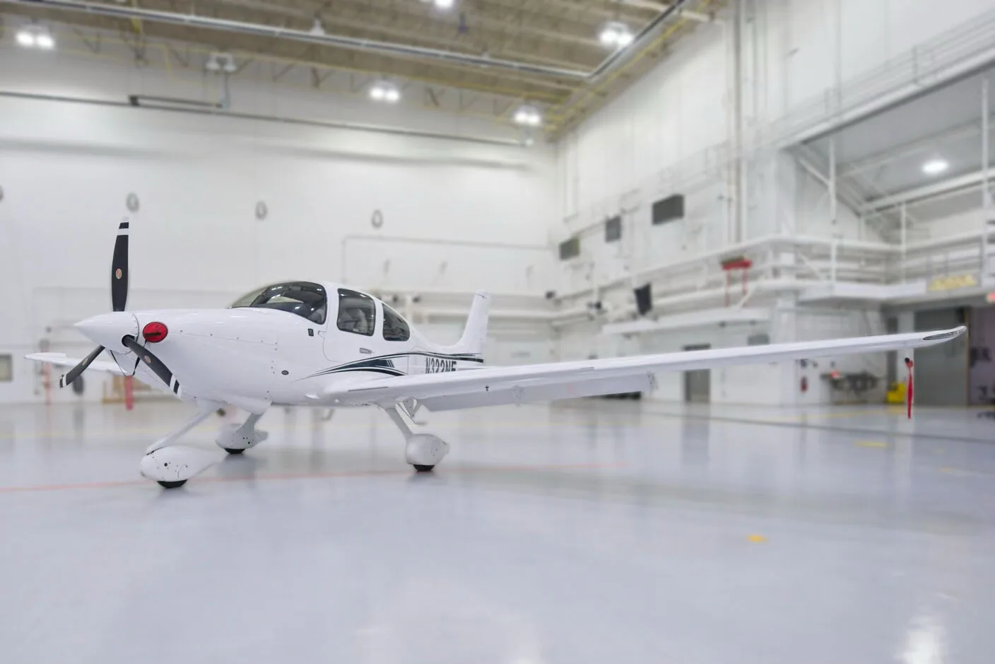 A front three-quarter view of a white Cirrus SR22 aircraft with black and blue stripes, N322NE, in a hangar.