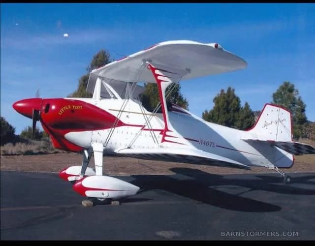 A red and white 'Little Toot' biplane, registration N40TL, parked on an asphalt tarmac under a clear blue sky.