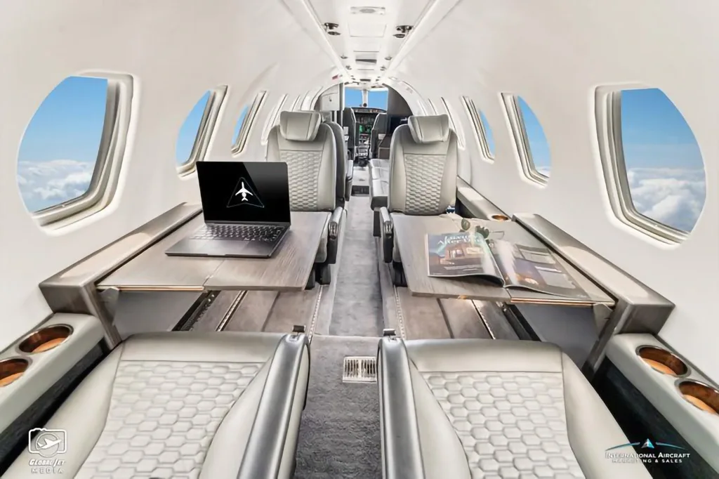 The luxurious cabin interior of the N15JT Cessna Citation X, featuring grey leather seats and tables.