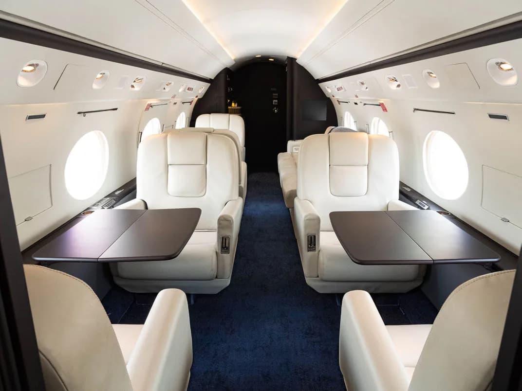 View of the aircraft interior with white leather seats and dark wood tables.