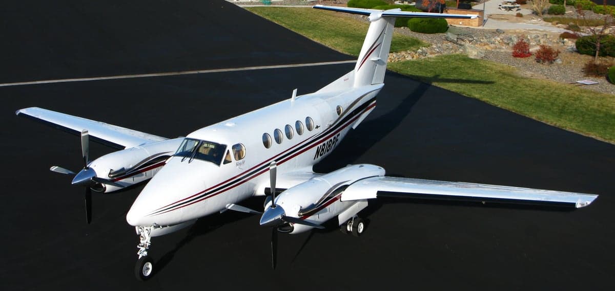 An elevated view of a white Beechcraft King Air with black and red stripes parked on an asphalt ramp.