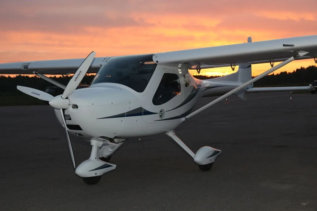 Front view of a white REMOS GX aircraft on the runway at sunset.