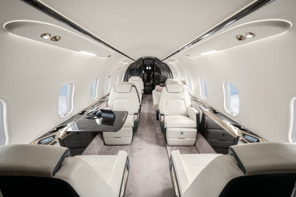 View of the aircraft cabin with white leather seats and dark wood accents.